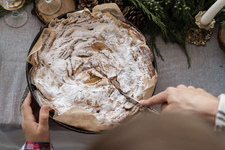 Christmas cupcake. A female hand cuts a Christmas homemade apple pie sprinkled with white powdered sugar. homemade cakes on a festive decorated tableの写真素材