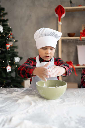 Children are cooking for Christmas. Boy baker in a cap and apron kneads flour for dough for gingerbread or cookies. process of making homemade cakesの写真素材