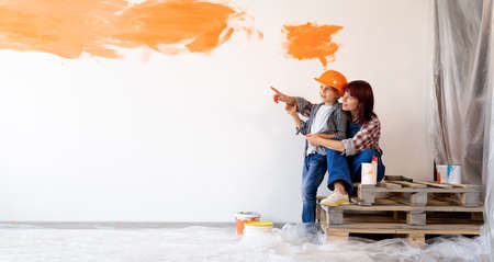 Mom and son are doing repairs in a new home. painted the wall orange. wall in the apartments with space for text. Loving mother hugging her sonの写真素材