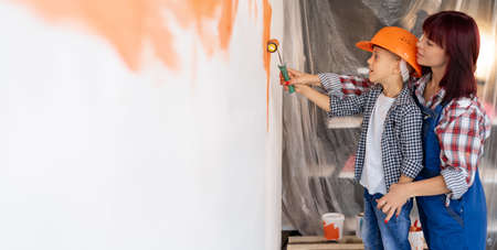 Home repairs. Mom helping her son paint the wall with a roller. The boy paints the wall of the apartment. New house renovation concept.の写真素材