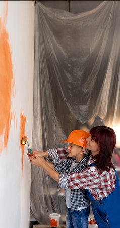 Mom and son are painting a wall in a new house. A woman teaches a child to paint with a roller while repairing an apartment. Home renovation concept.の写真素材