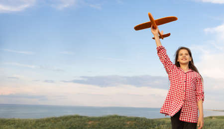 Child girl launches a toy plane into the sky. The child dreams of flying. Little stewardess in nature. Sunset sky background. Active rest concept.の写真素材