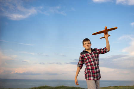 child pilot aviator dreaming to travel launches a toy airplane at sunset. Boy on a background of blue sky flying an airplane. An active walk in natureの写真素材