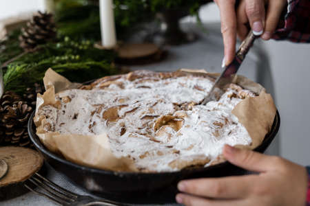 Christmas cake. A hand with a knife cuts a Christmas homemade apple pie sprinkled with white powdered sugar. homemade cakes on a festive tableの写真素材