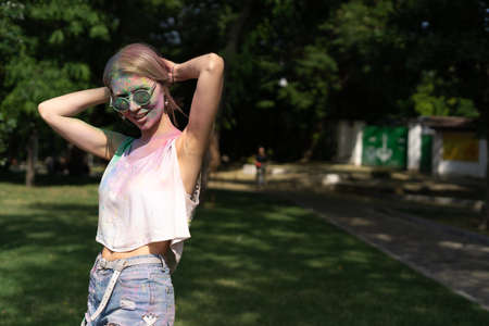 Holi Colors Festival. Portrait of a happy young beautiful girl at the Holi festival. Blonde girl in the park with a dirty face. Colorful powder paintの写真素材