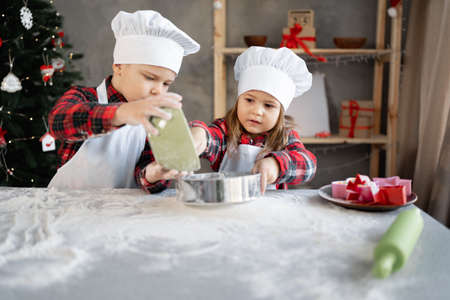 children brother and sister sift flour for Christmas cookies or gingerbread dough. Childrens culinary blog baking section. Little bakersの写真素材
