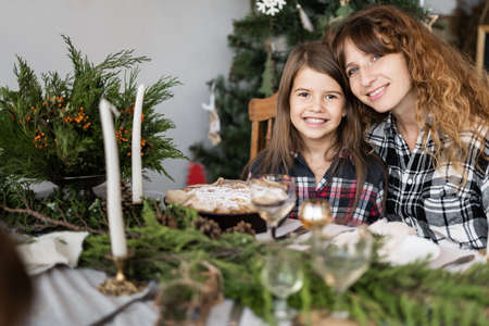 Family at Christmas at the festive table. Portrait of a happy mother and daughter at a decorated table in the living room. Candles, twigsの写真素材