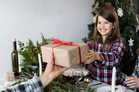 Merry Christmas. Happy little girl with a gift box at the festive table. Family holiday Christmas dinner at a decorated table.の写真素材