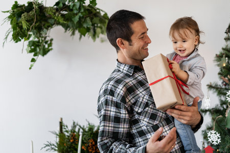 Family at Christmas at home, dad giving the kid a gift box in the morning. Dad holds a little boy in the living room. Home New Year concept.の写真素材