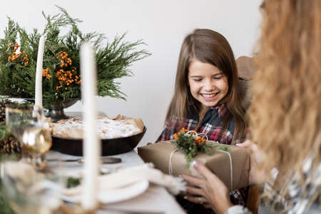 Christmas morning, mom gives her daughter a gift sitting at the festive table at home. Celebration atmosphere. Christmas and New Year at home.の写真素材