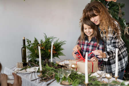 Happy family mom and daughter open a Christmas gift box at the festive table. Celebrating Christmas morning at home. X-mas concept. Background.の写真素材