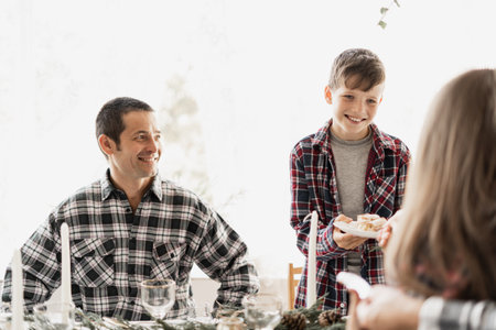 Dad and children at the Christmas table. Family Christmas breakfast. The girl treats her brother to a cake or cupcake. Concept new year at home.の写真素材