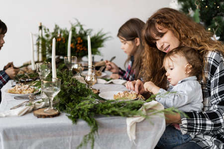Mom and the kids have breakfast on Christmas Day at a festive decorated table in the bright living room in the morning. The family eats at the tableの写真素材