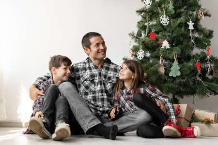 Close-up of a happy family under a tree for Christmas or New Year. Dad with his son and daughter on the floor x-mas in the morning.の写真素材