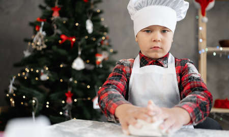 Portrait of a little baker in uniform making bread dough. Boy prepares cookies or gingerbread for Christmas. The child makes pizza dough.の写真素材