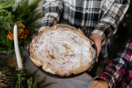 Christmas cake in the form. Female hands hold the shape with an apple pie. Homemade cakes with powdered sugar. Bake for Christmasの写真素材