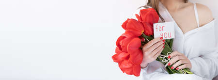 Girl with red flowers on a white background. Tulips and a postcard for you in hand. Banner.の写真素材