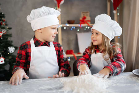 Happy brother sister make dough for Christmas cookies, children in the kitchen are preparing gingerbread cookies, little cooks. Christmas foodの写真素材