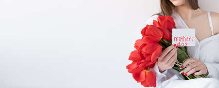 Flowers for Mothers Day. Girl with tulips and a postcard on a white background. Happy mothers day. Bannerの写真素材