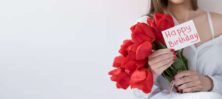 Flowers for Happy Birthday. Girl with tulips and a postcard on a white background. Happy holiday. Flower delivery. Celebrate concept. Banner.の写真素材