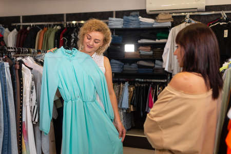 girl trying on a dress in a clothing store, her friend advises, womens shopping in a boutique, department of a shopping center with clothes.の写真素材