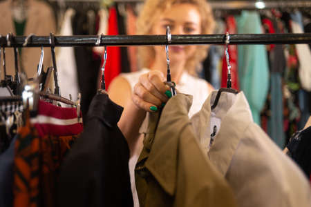 woman buyer choosing clothes in a store, blonde looks at a coat in a boutique on a hanger, selling things in a warehouse, female shopping at a saleの写真素材