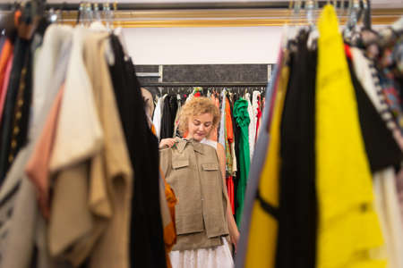Shopping at the market or clothing store. Woman shopper trying on a shirt. Big sale of goods. Clothes rows with hangers. Shopaholic addiction.の写真素材