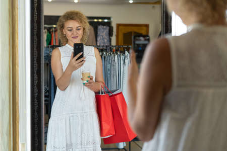 a regular customer of a clothing store, a woman makes a selfie with purchases in front of a mirror, a sale in a fashion boutique, a shop ownerの写真素材