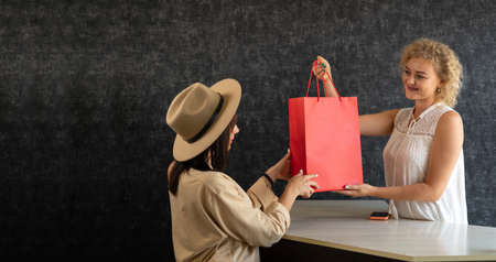 Girl shopper in a clothing store with a paper bag, a seller of the clothing department giving a customer a purchase in a red package, shopping.の写真素材