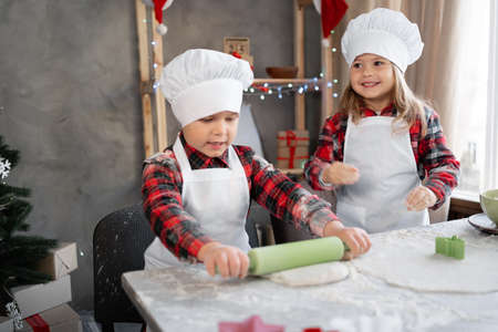 two children rolling out dough on christmas cookies at home in the kitchen, brother and sister making cookies or gingerbread, christmas.の写真素材