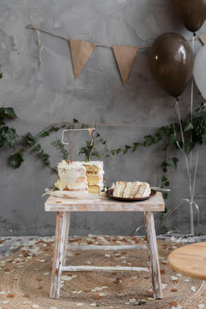 Decorated with cream cake for the first Birthday standing on a small wooden table, a cut piece of cake on a plate, a room with handmade decorations.の写真素材