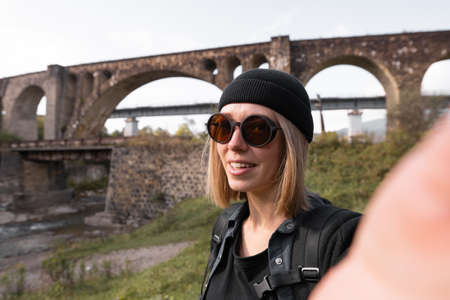 Girl blogger leading a live broadcast of the old arched stone bridge of the railway, a tourist on a journey leading a video blog about of bridgesの写真素材