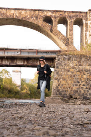 Arched old stone bridge, girl tourist walking by the river, hiking trekking, railway bridge background, tourism and travel.の写真素材