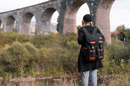 Girl tourist looks at the old arch bridge, traveler traveling through Europe, young woman in an unusual place, back view. Nine-arch bridge.の写真素材