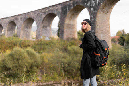 Girl traveler near the old arch bridge traveling through Europe, stone bridge on the background, tourist on a trip in nature.の写真素材