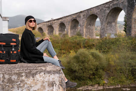 Traveler girl looks at the arched old stone bridge, sitting opposite, the lifestyle of a tourist, traveling across the bridges.の写真素材
