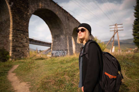 girl traveler near the old stone bridge of the railway, arched historical bridge in travel across europe, tourist on the background of the cloudy skyの写真素材