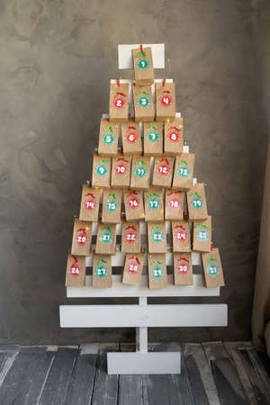 Handmade advent calendar presents in craft bags hanging on a wooden Christmas tree. Creative present with numbers for children for the new yearの写真素材