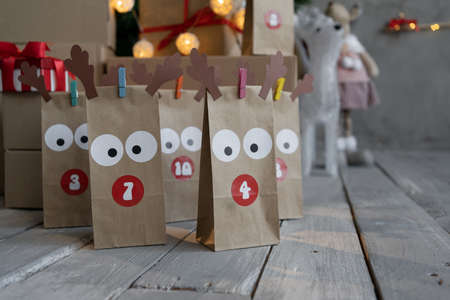 Christmas advent calendar, gifts in a craft bag standing on a wooden floor. Natural materials for homemade gifts. Festive background with garland.の写真素材