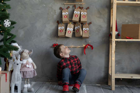 Small gift craft packaging advent calendar hanging on the wall, boy looking at gifts Christmas advent calendar, crafts for children.の写真素材