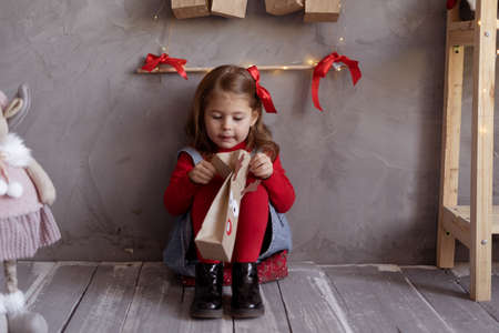 Happy girl opening package with advent calendar on Christmas eve, child sitting on floor in childrens room with craft present of sweets.の写真素材