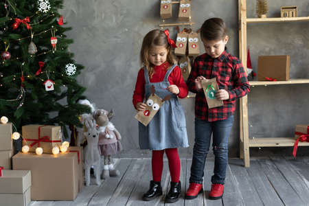 Handmade advent calendar packages in childrens hands, crafts for Christmas, happy kids brother and sister on Christmas eve with package number oneの写真素材