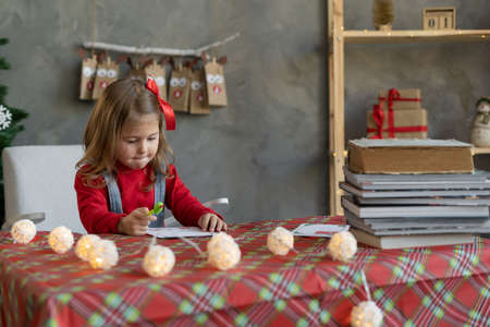 Little girl writes a letter to Santa Claus while sitting at the table at home, child on Christmas eve handwritten list of gifts.の写真素材