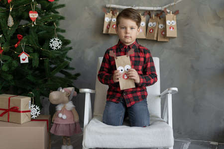 Happy little boy holding packages of sweets advent calendar, christmas kids fun, child at home waiting for the holiday, concept kids advent calendarの写真素材
