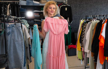 girl in a clothing store trying on a pink dress, a woman chooses a summer dress for sale, a customer in a womens showroom, seasonal shopping.の写真素材