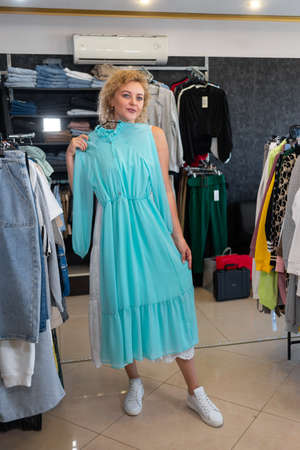 shopping concept, blonde girl chooses a dress in a clothing store, buying womens clothing, trying on in a store. Clothes background.の写真素材