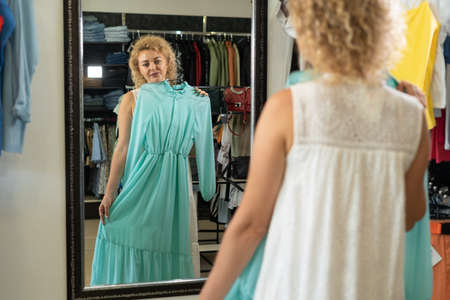 Woman trying on dress in front of mirror in boutique, fitting room in clothing store, womens clothing department of shopping mall.の写真素材