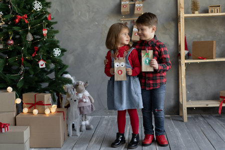 Paper bags with advent calendar in childrens hands, Christmas handmade crafts, brother and sister with package number 1, christmas tradition.の写真素材