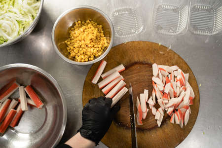 cook crab salad with corn in the kitchen, chefs hands cut a crab stick with a knife, restaurant food cooking process, top view. Chef preparesの写真素材