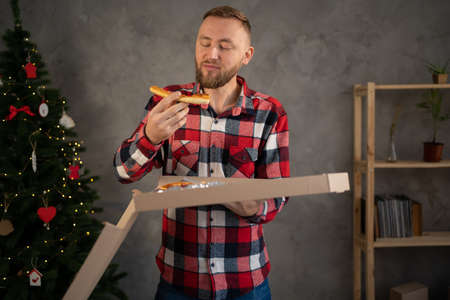 pizza delivery home, man eating a slice of pizza holding a box, christmas at home alone, christmas food deliveryの写真素材